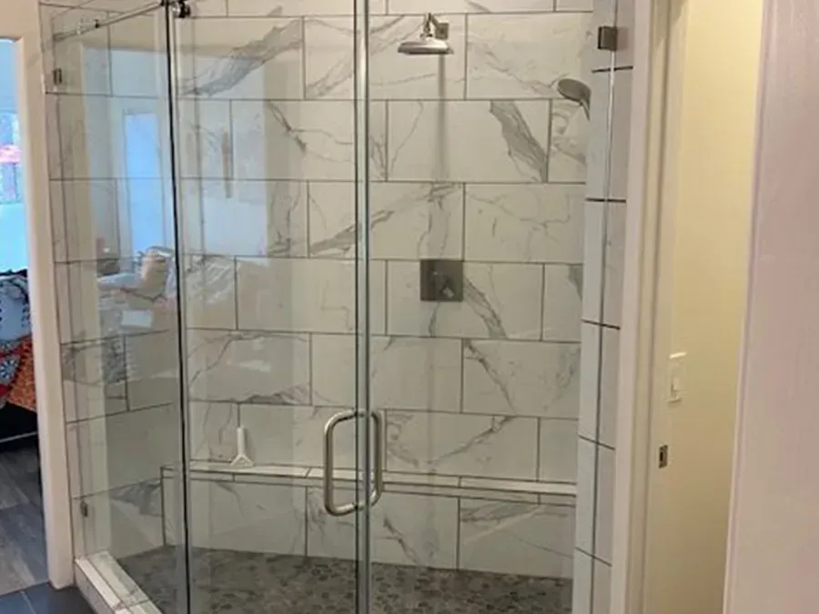 Glass shower enclosure with marble-look tile and chrome handles in a bathroom