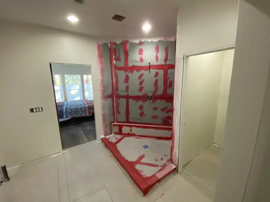 Bathroom under renovation with pink waterproofing on walls and floor, doorway to a tiled room visible.