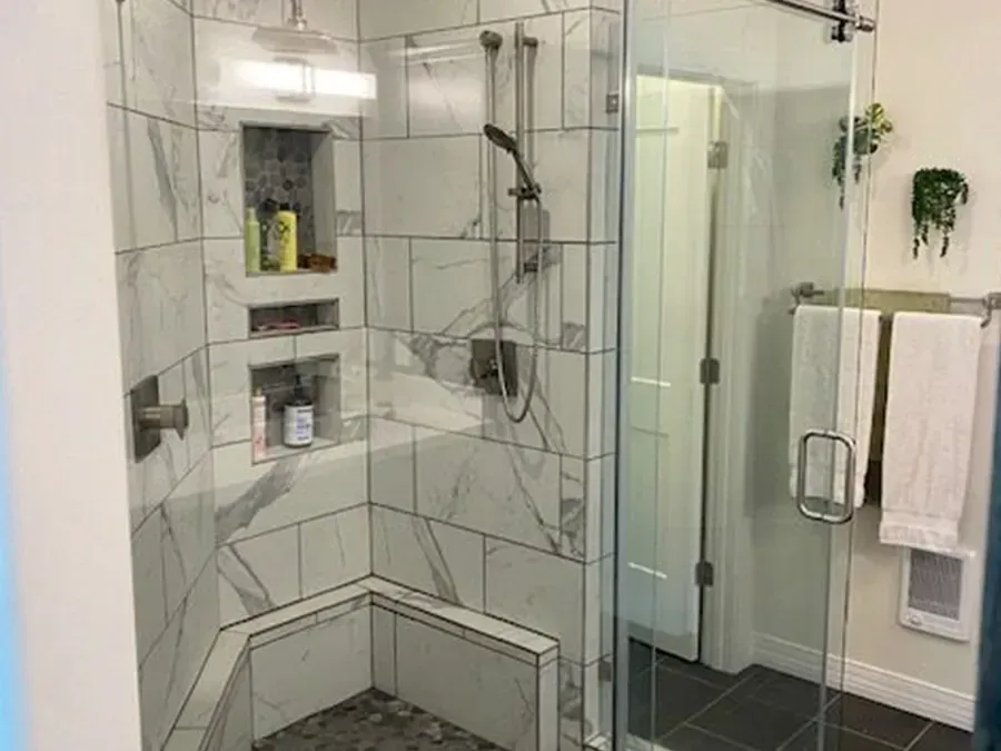 Glass-tiled walk-in shower with built-in shelves, bench, and chrome fixtures in a bathroom