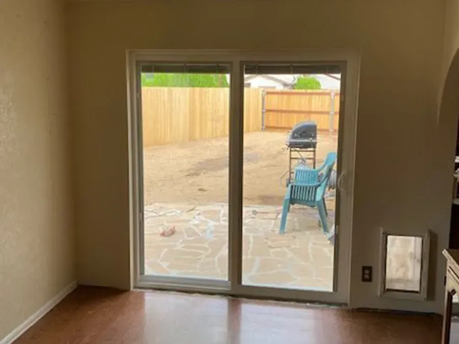 Empty room with sliding glass doors opening to a patio with two chairs and a grill.