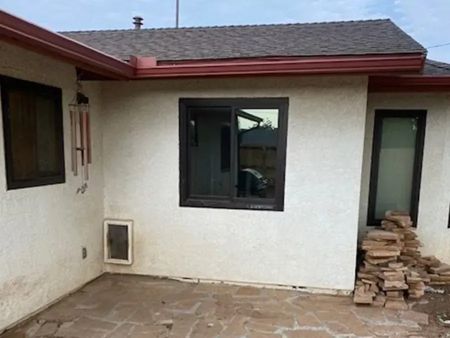 Backyard patio with stucco house wall, windows, and a pile of stacked pavers.