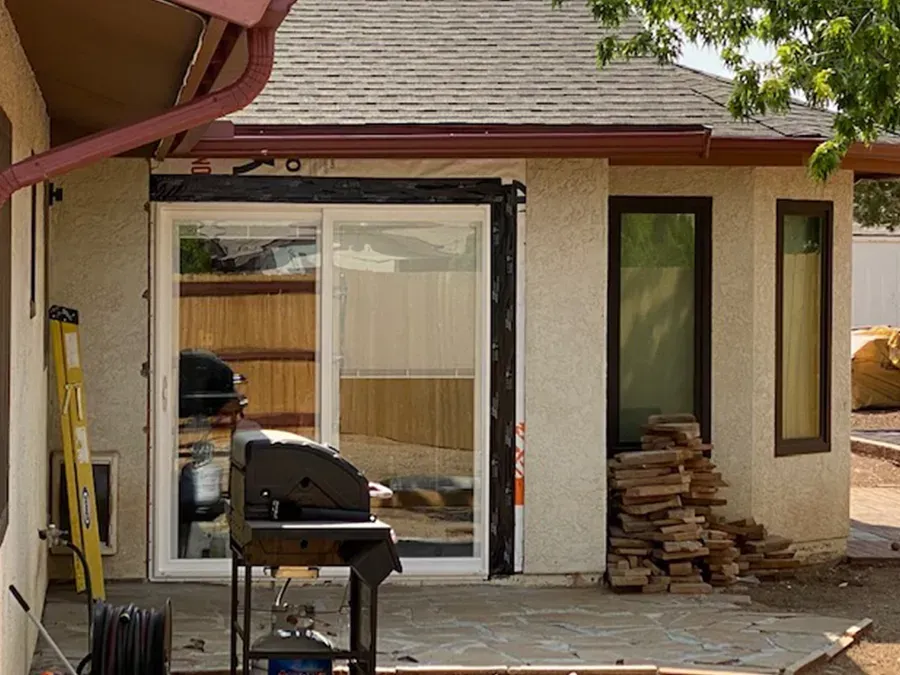 Back patio with a barbecue grill beside sliding glass doors and stacked firewood by the wall