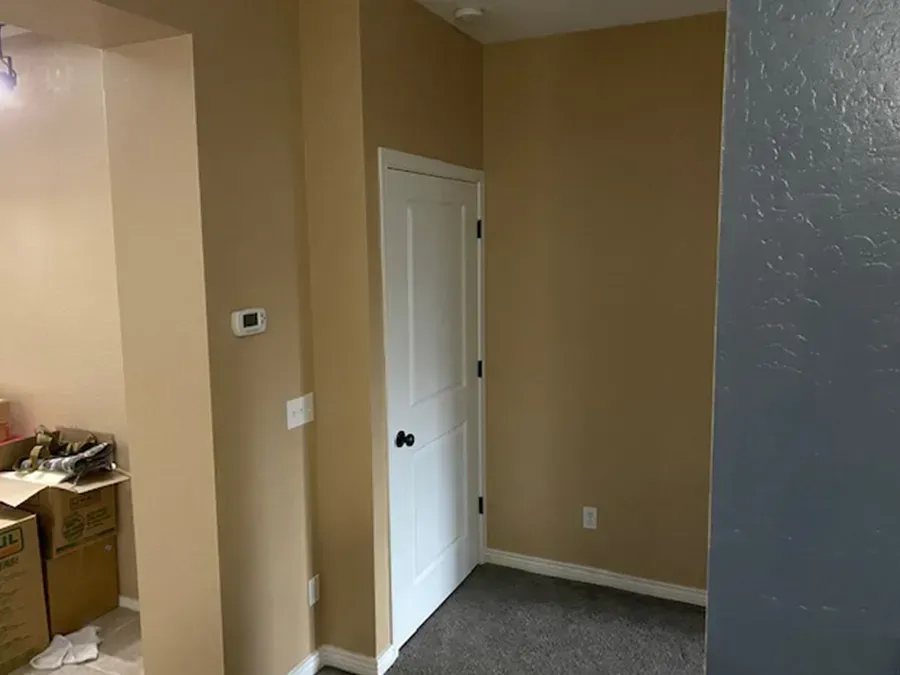 Empty hallway with beige walls, white door, and gray carpet in a home interior