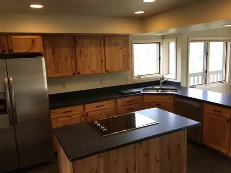 Modern kitchen with stainless steel fridge, wood cabinets, dark counters, and a central island