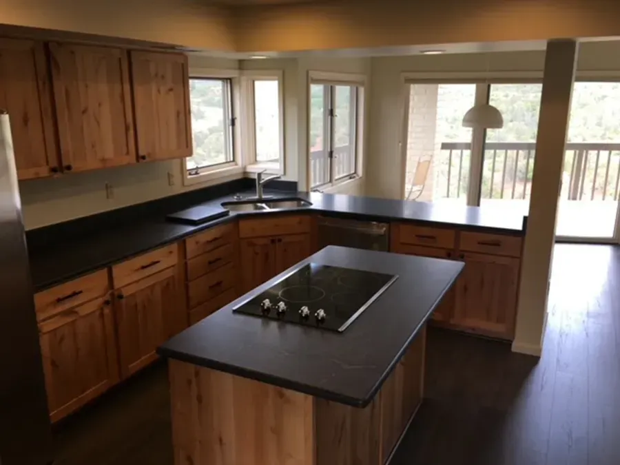 Modern kitchen with wood cabinets, black countertops, center island, and large windows overlooking a deck