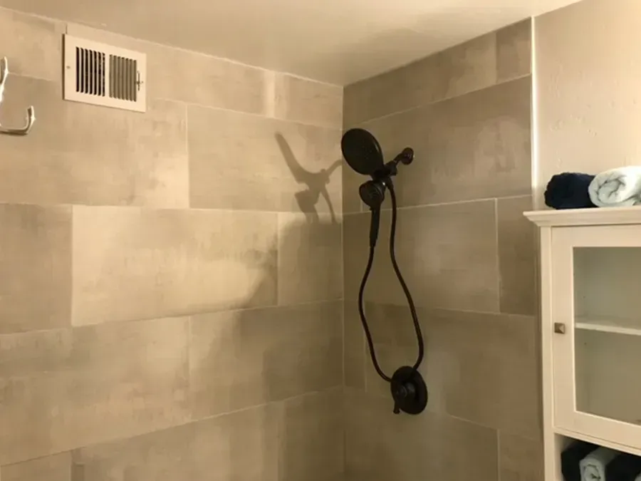 Tiled shower with black handheld showerhead, wall vent, and white cabinet edge in view