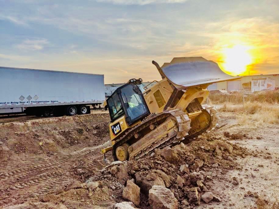 A bulldozer is stuck in the dirt next to a semi truck.