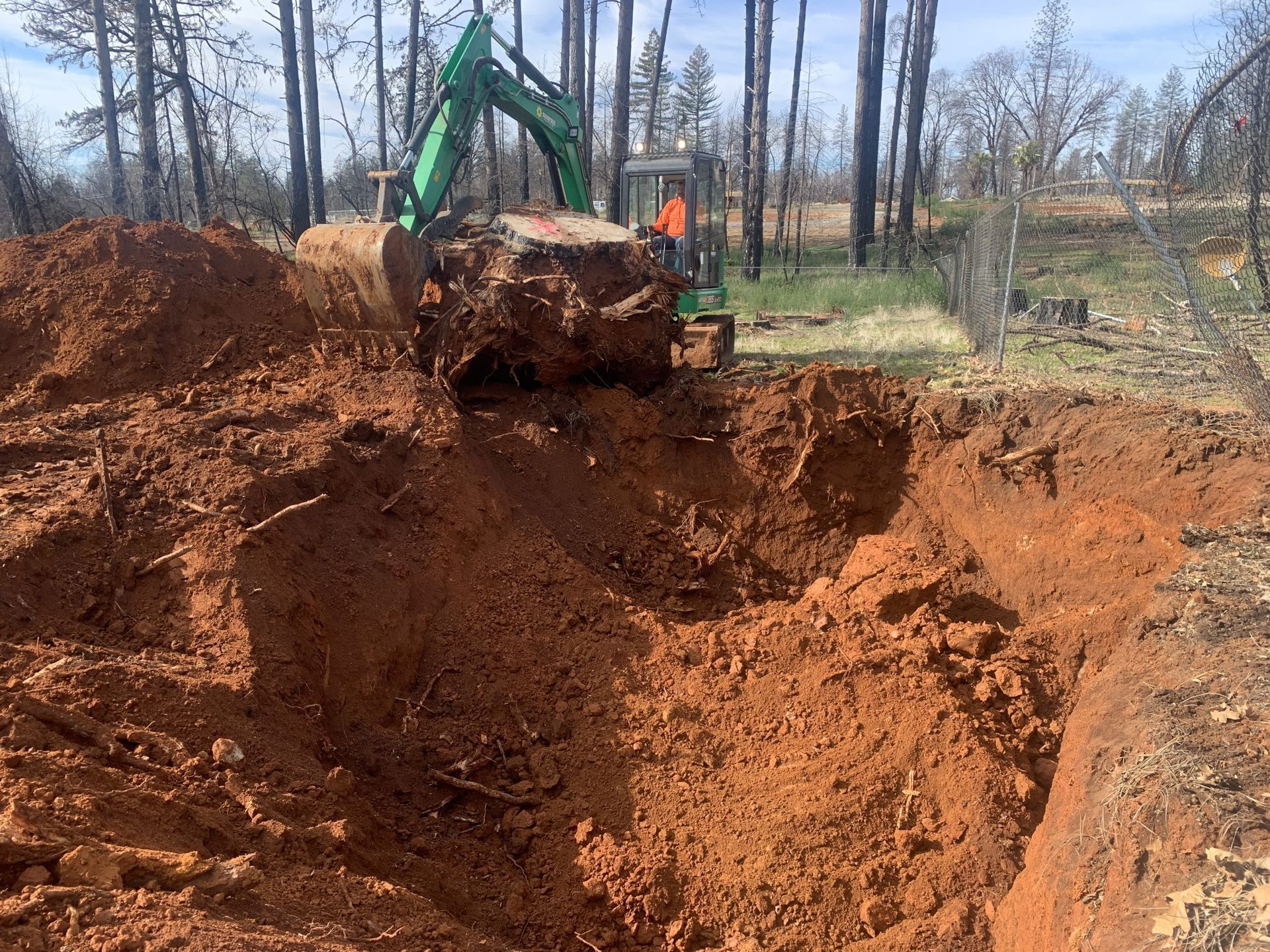 A green excavator is digging a hole in the dirt.