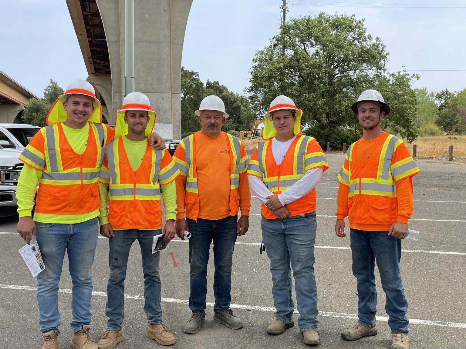 A group of construction workers wearing orange vests and hard hats are posing for a picture.