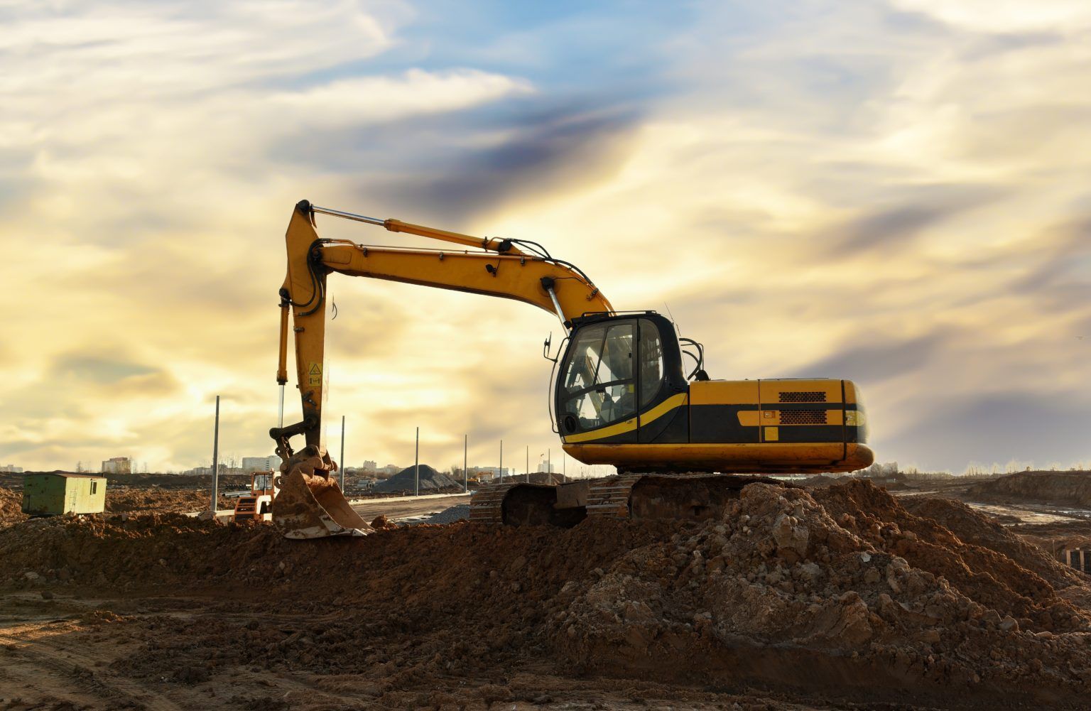 A yellow excavator is sitting on top of a pile of dirt on a construction site.
