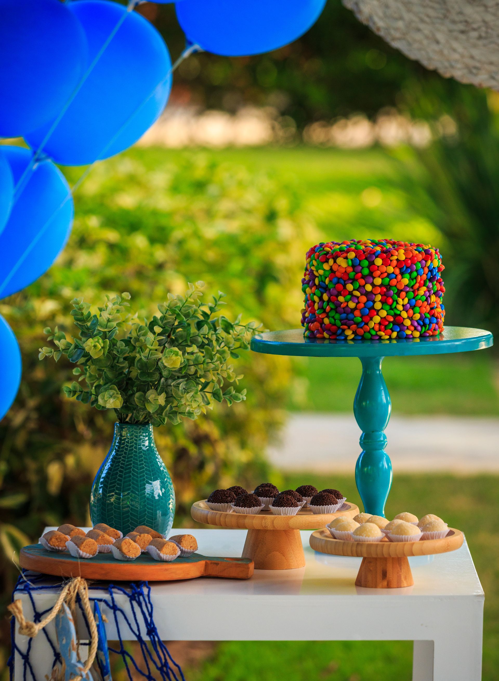 Uma mesa com um bolo e cupcakes e balões azuis ao fundo.