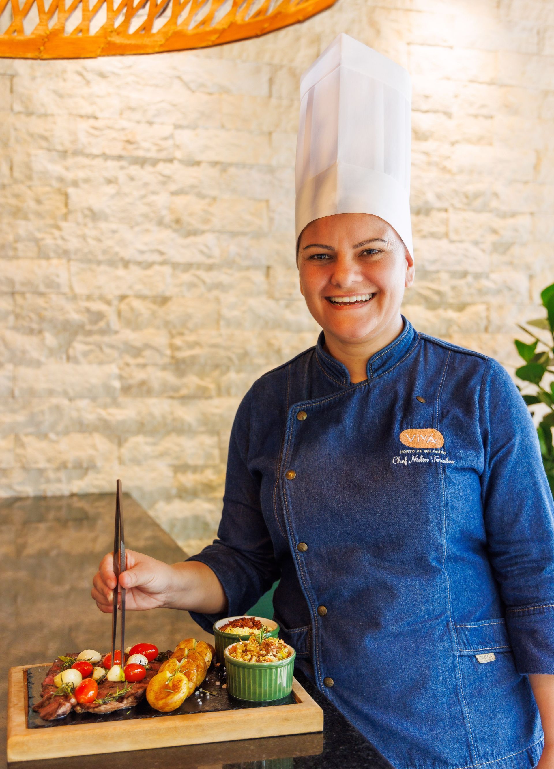 Uma mulher com chapéu de chef segura uma bandeja de comida.
