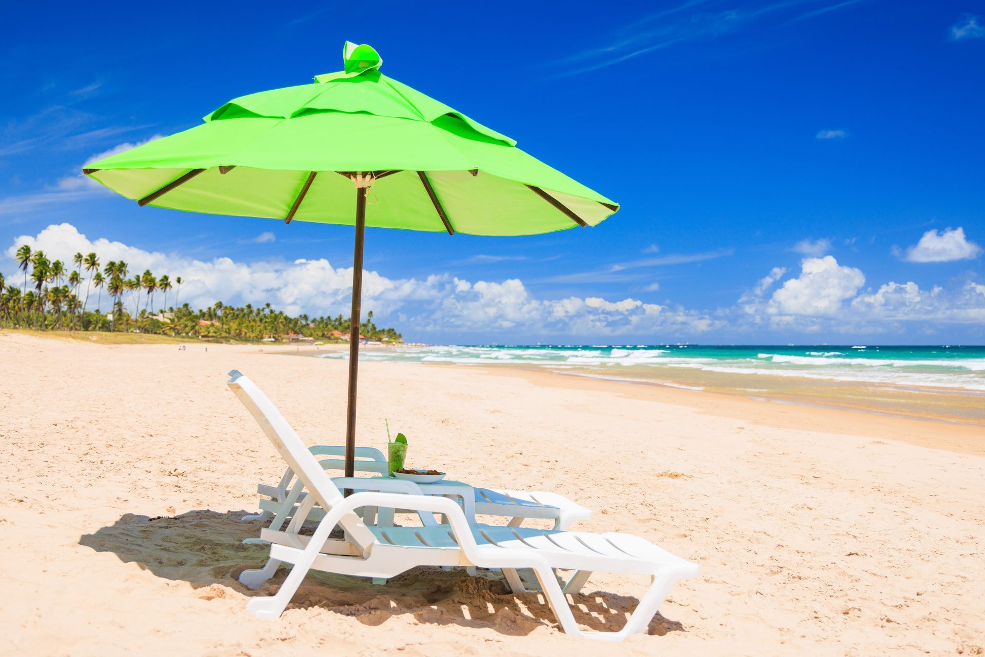 Uma praia com um guarda-sol verde e cadeiras