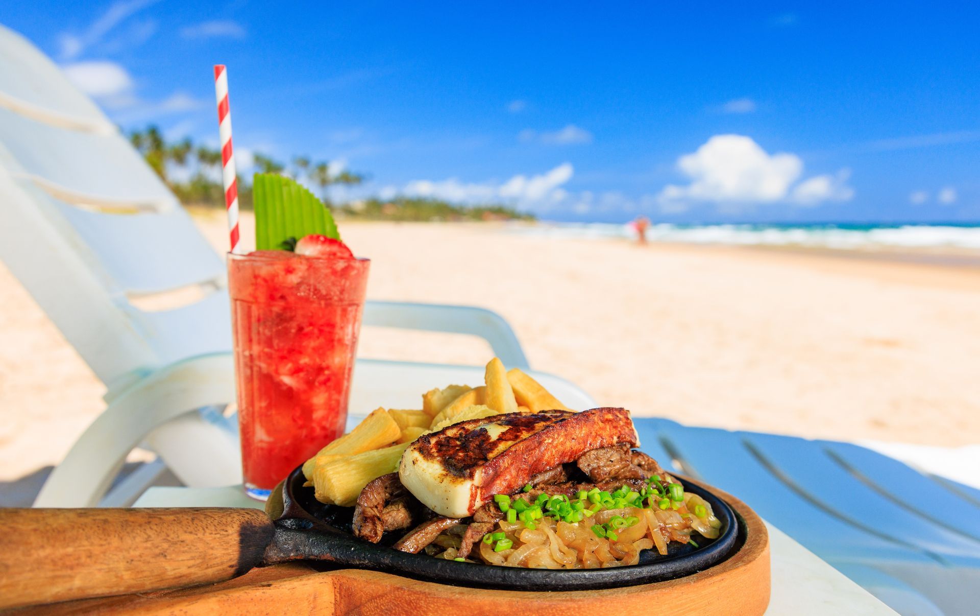 Há um prato de comida e uma bebida na praia.