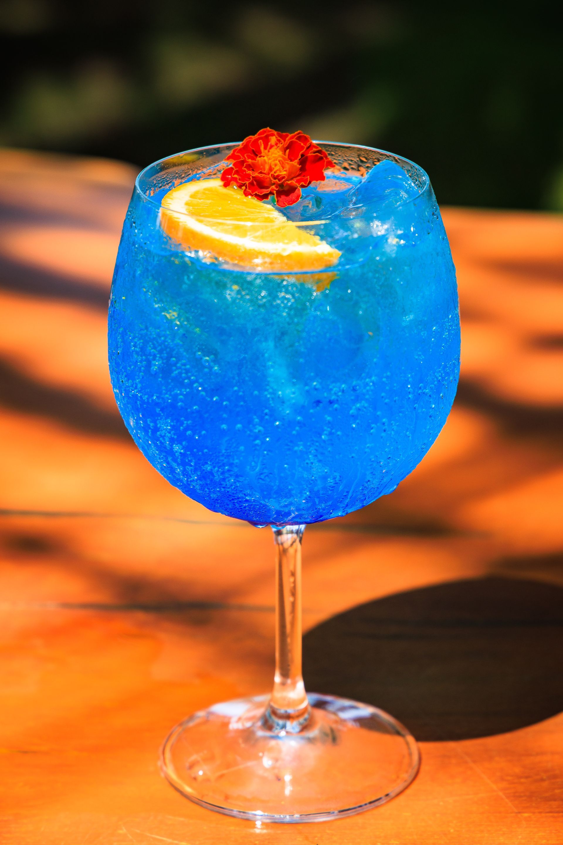 Uma bebida azul em uma taça de vinho com uma rodela de limão e uma flor no topo.