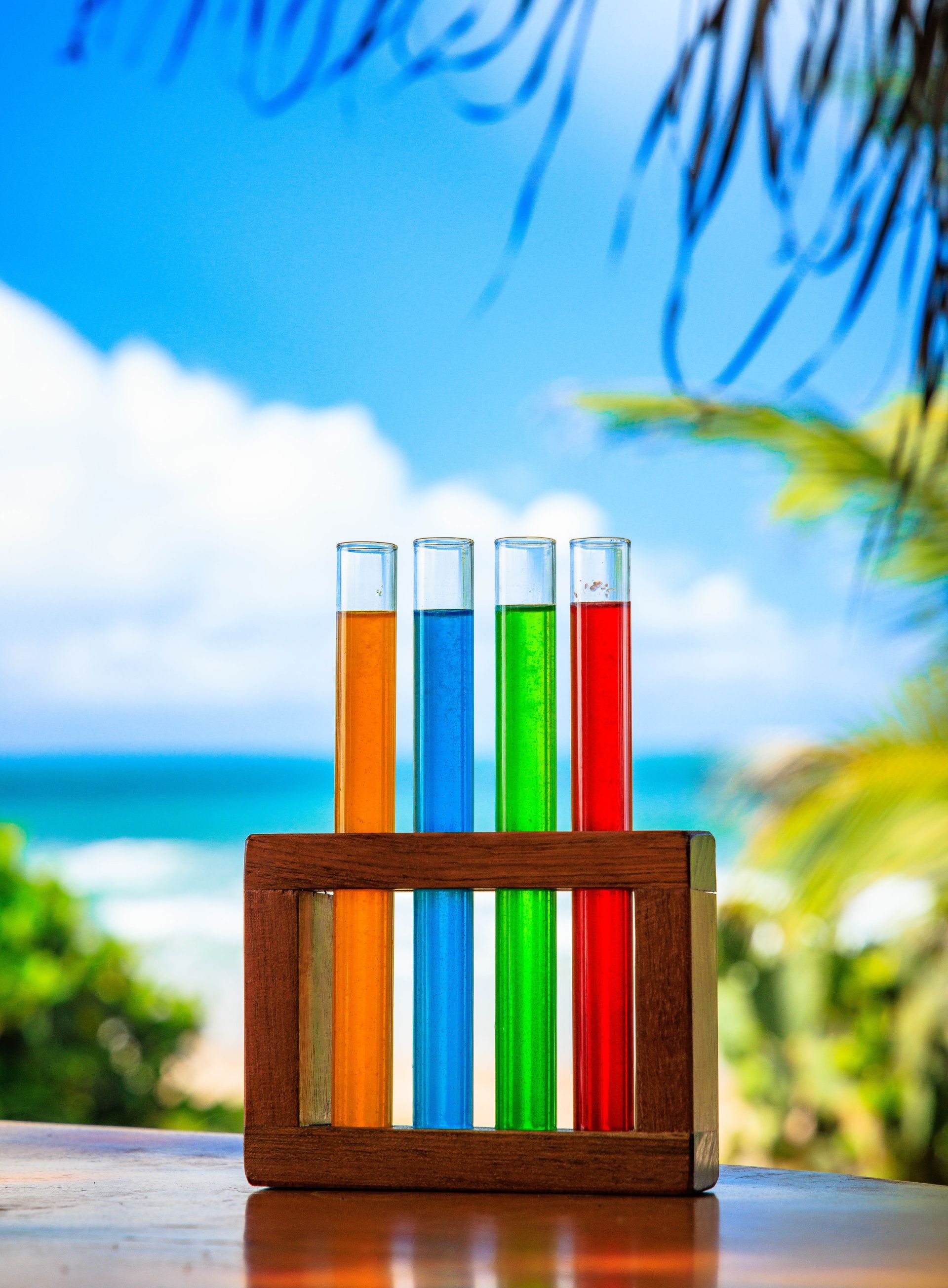 Quatro tubos de ensaio cheios de líquidos de cores diferentes estão sobre uma mesa de madeira.