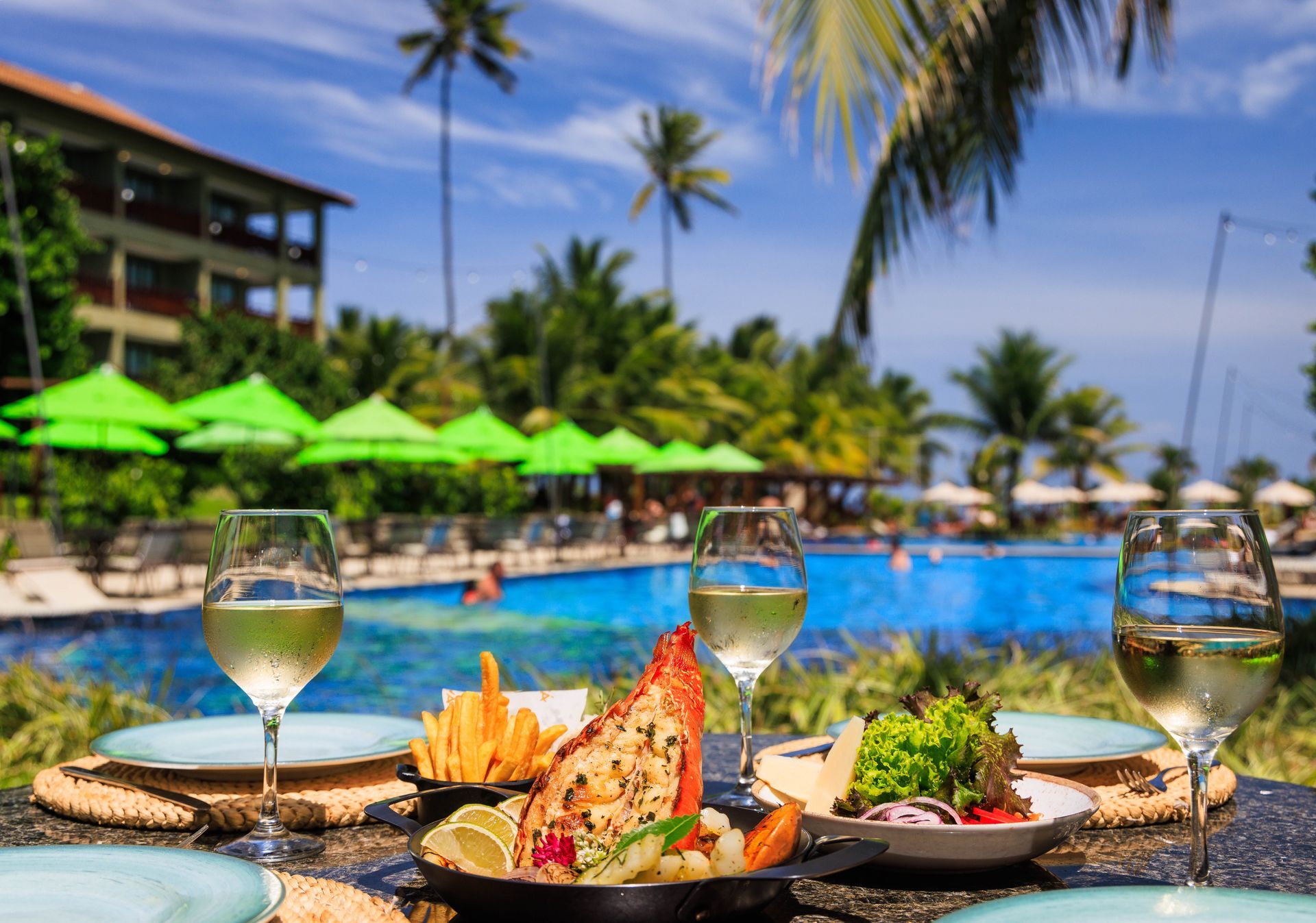 Uma mesa com pratos de comida e taças de vinho em frente a uma piscina.