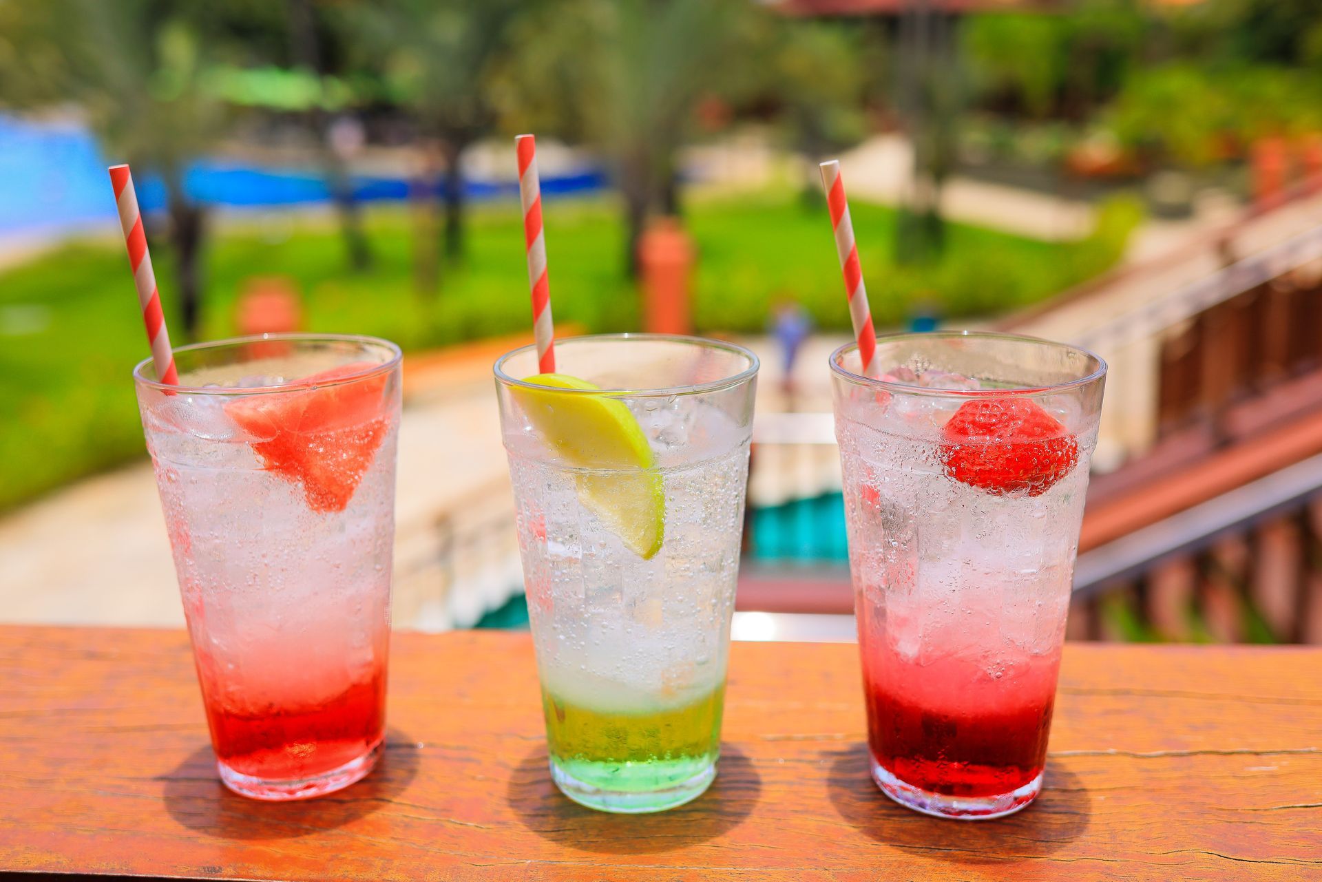 Três copos de bebidas de cores diferentes com canudos sobre uma mesa de madeira.