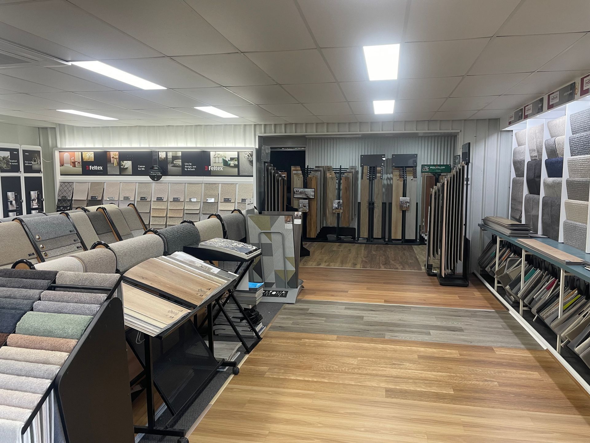 Interior of a flooring store showcasing various carpet and tile samples, with wood flooring on the ground.