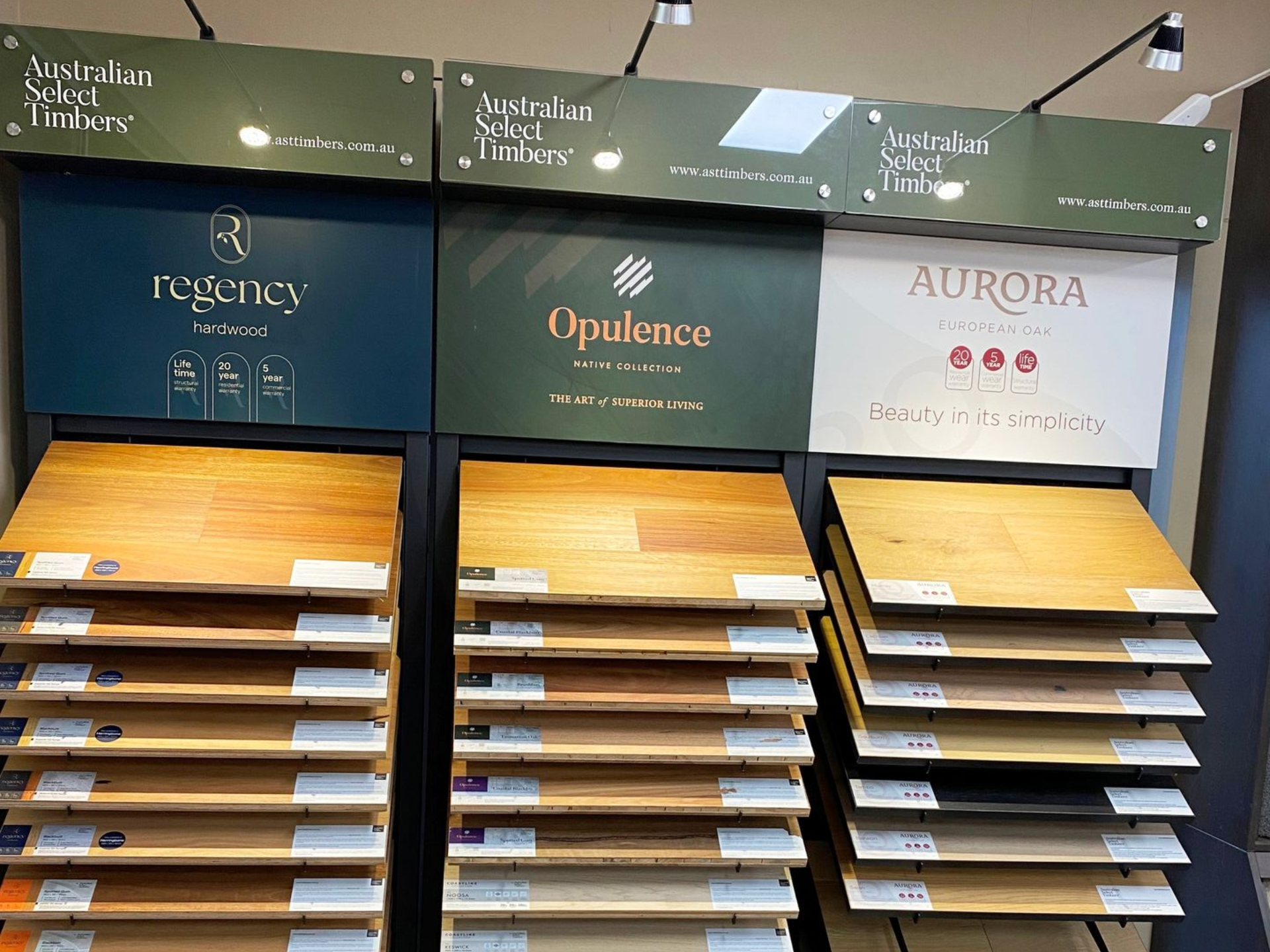 Display of wooden flooring samples from three brands: Regency, Opulence, and Aurora, showcasing various colors and grains.