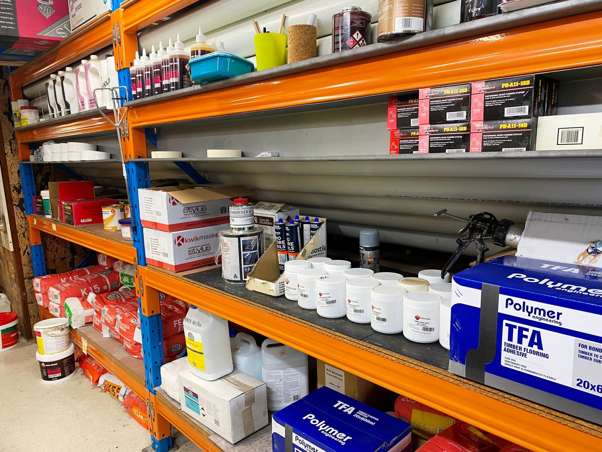 Shelves of construction supplies in a storage area. Orange shelving, various boxes and containers.
