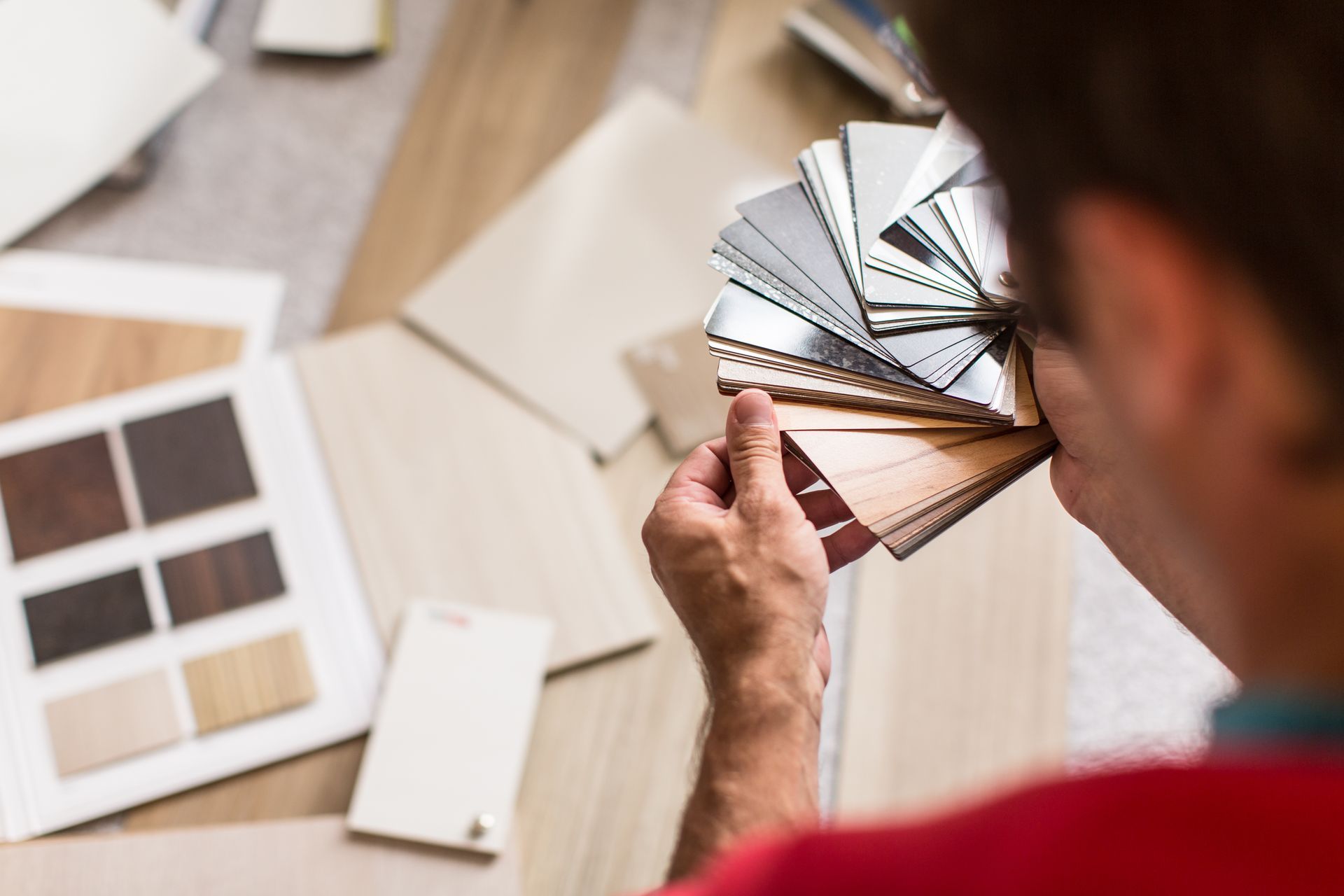 Person holding a color swatch fan, comparing it to flooring samples on a surface.