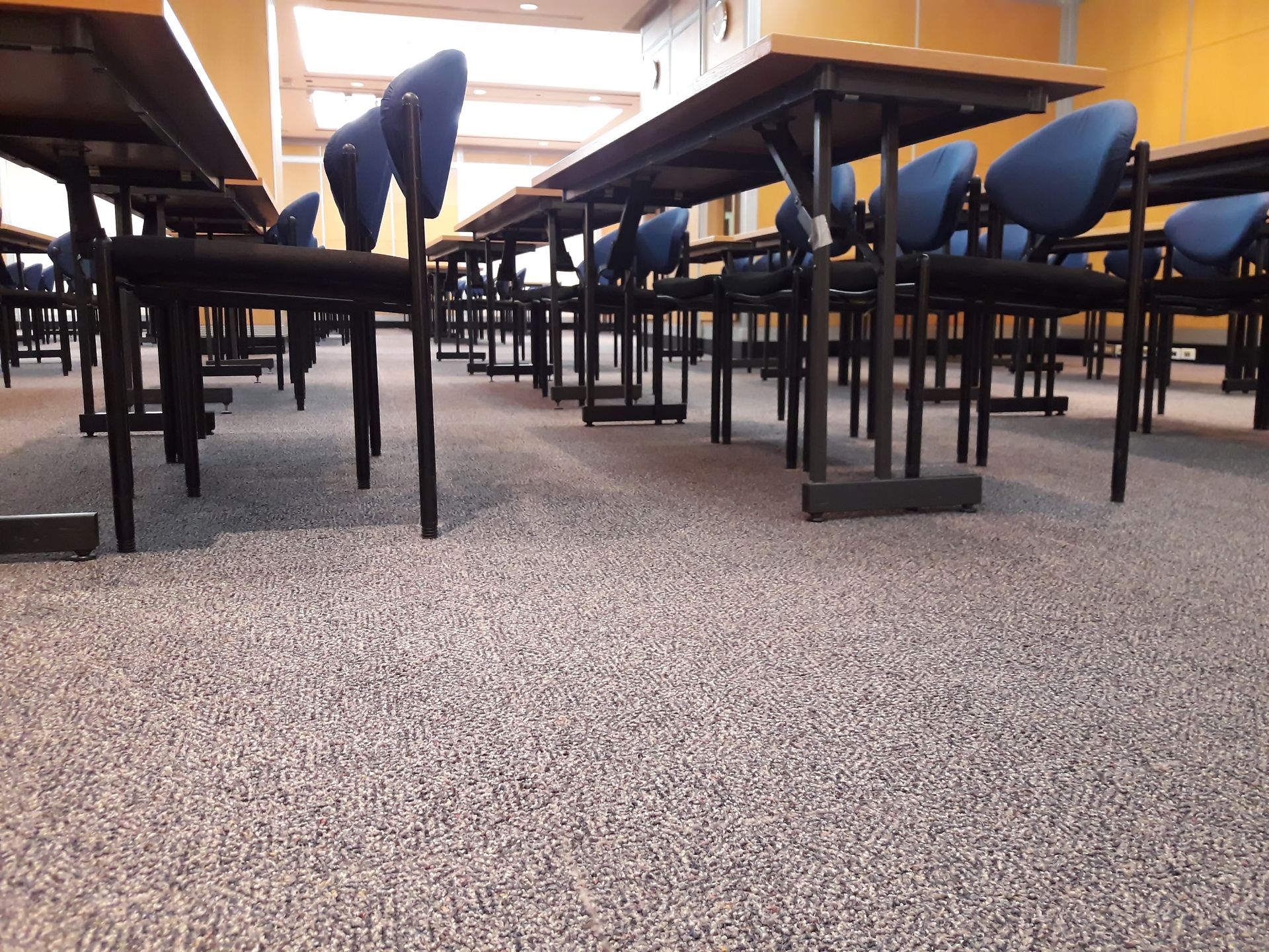 Rows of desks and chairs in an empty classroom, a mottled gray floor, and yellow walls.
