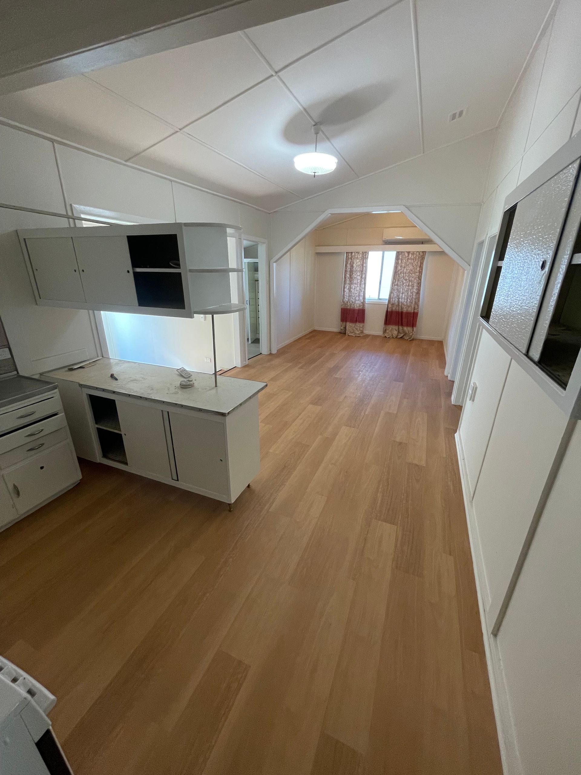Interior view of a room with light wood floors, white cabinets, and a window with red curtains.