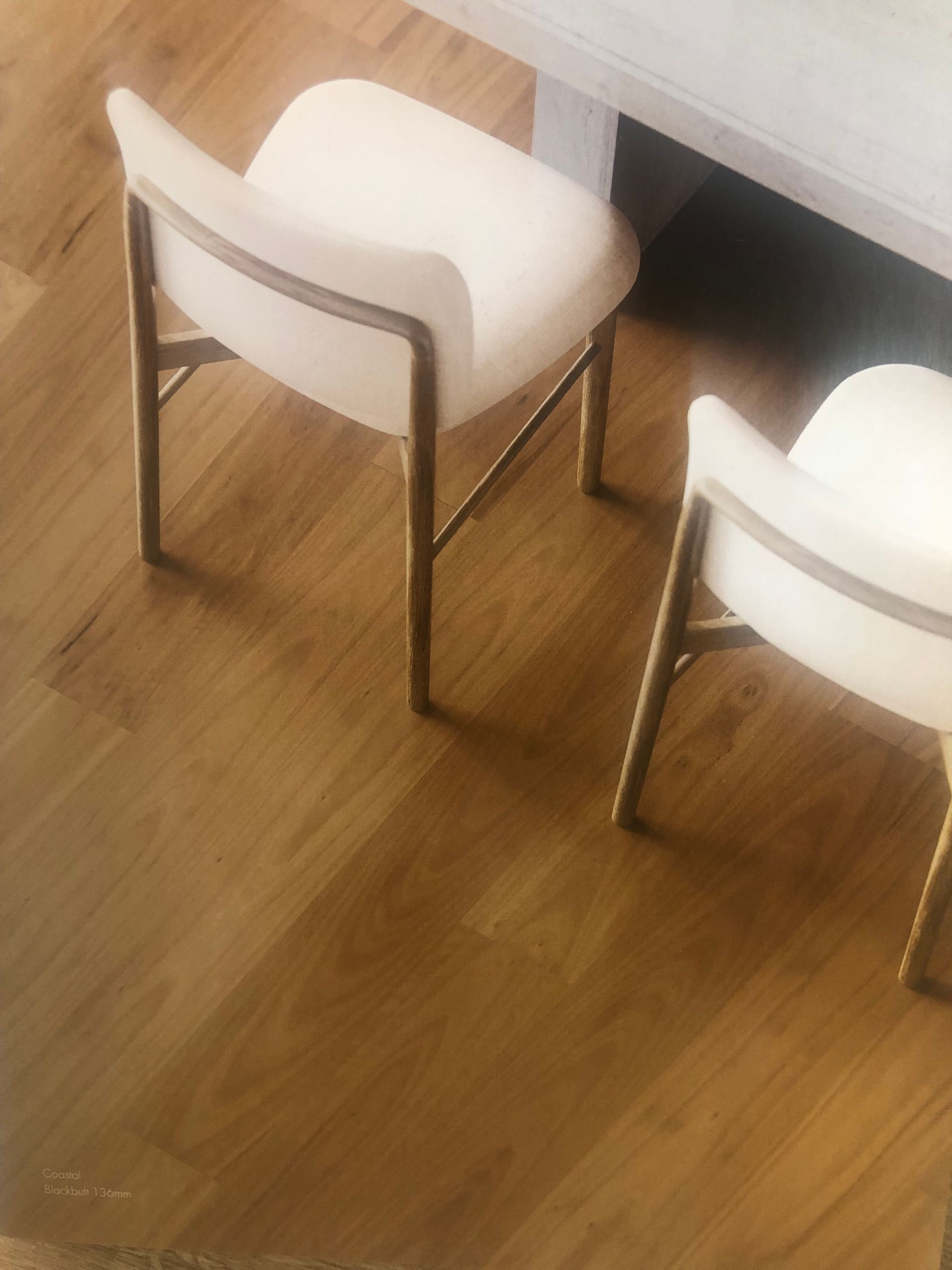 Two white cushioned chairs with gold frames sit on a wooden floor near a table leg.