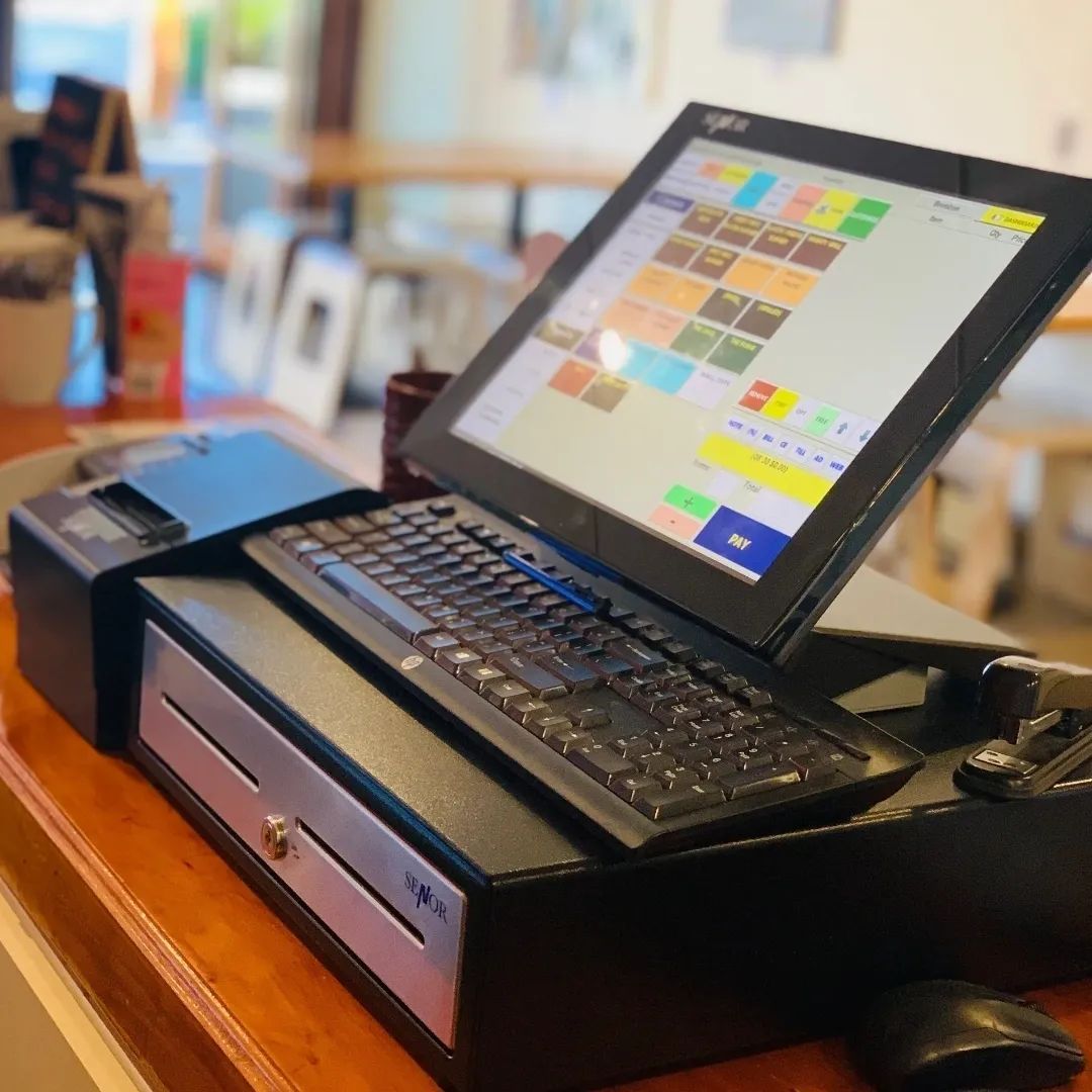Point-of-sale system on a counter with a cash register, keyboard, and screen displaying menu items.