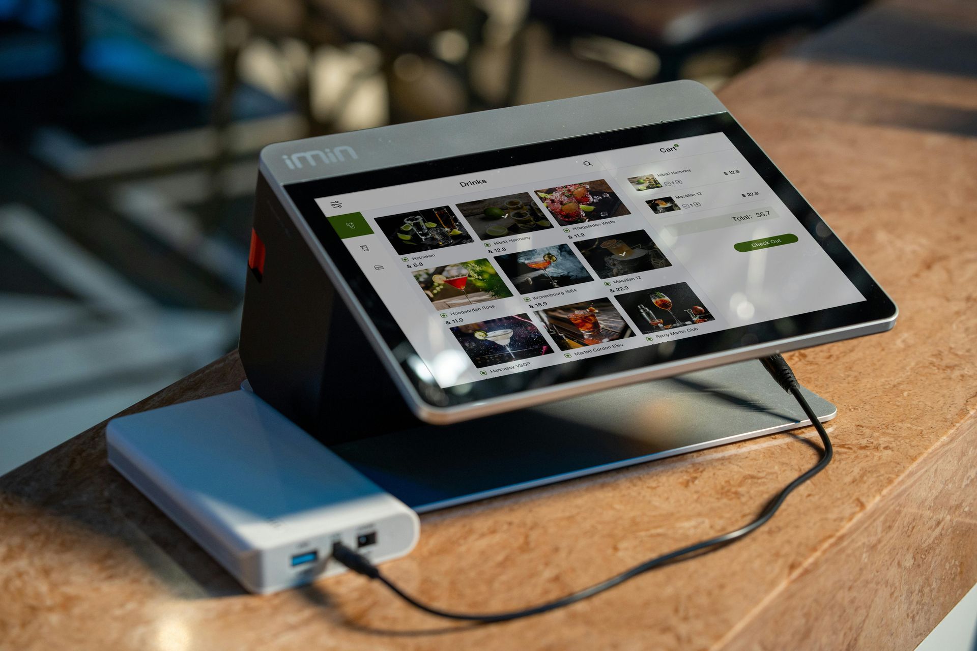 Gray tablet POS system charging from a white portable charger on a wooden counter.