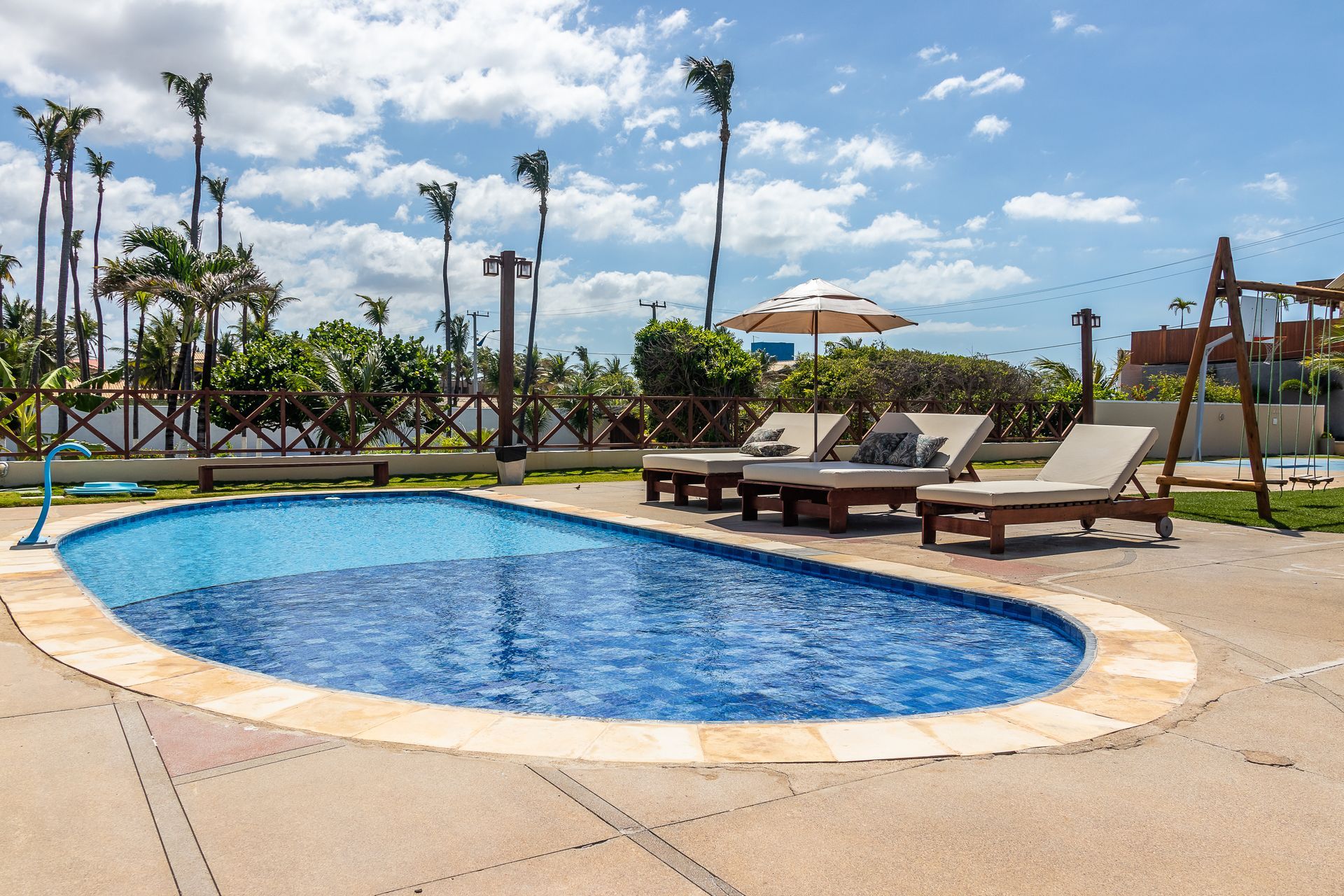 Swimming pool with lounge chairs under a sun umbrella on a sunny day.