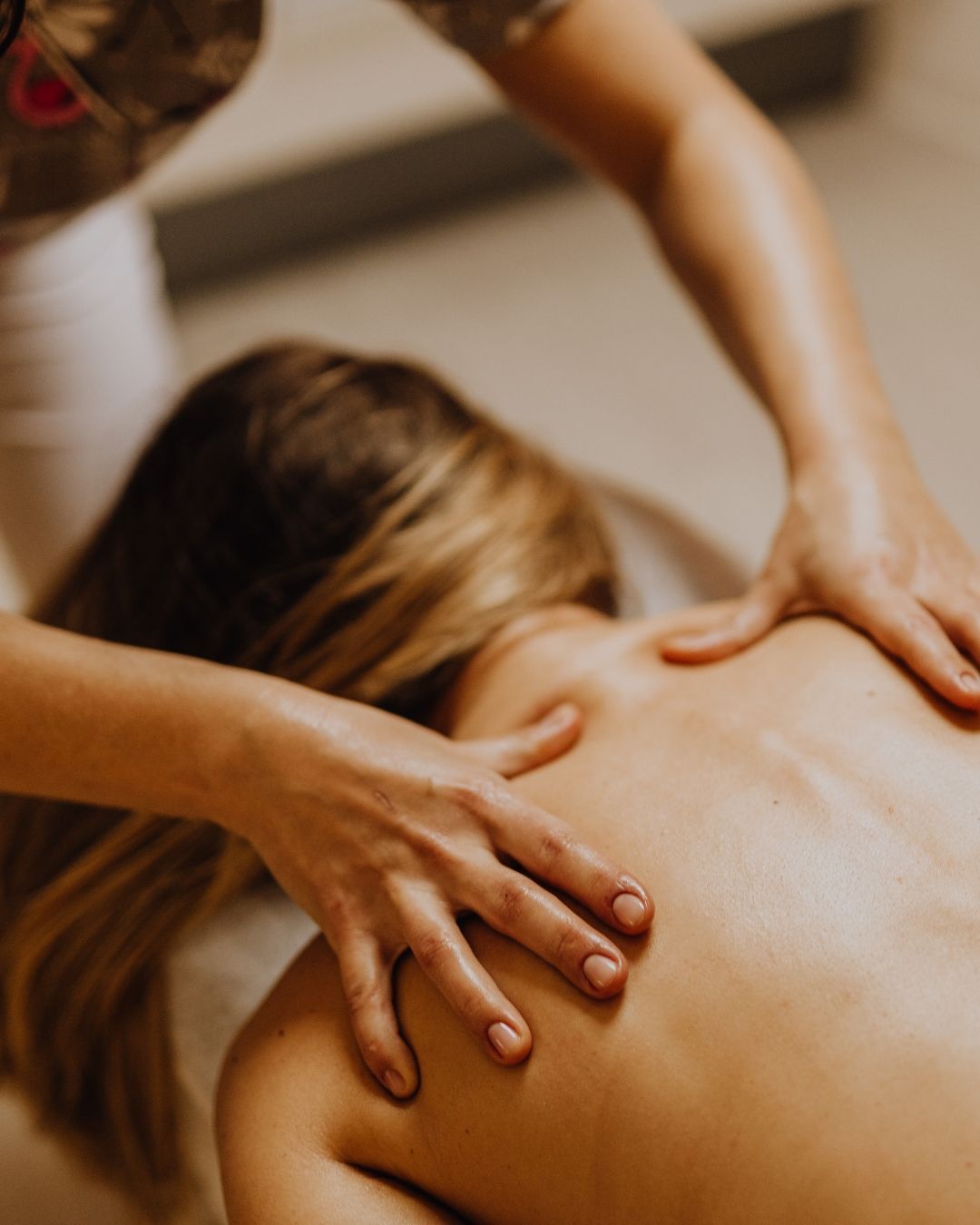 Person receiving a back massage with hands on the shoulders, indoors.