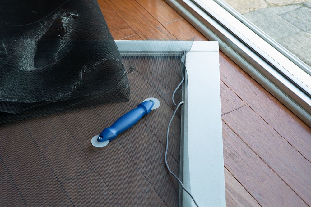 Screen door frame with replacement screen and roller tool on hardwood floor.