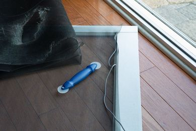 Screen door frame with replacement screen and roller tool on hardwood floor.