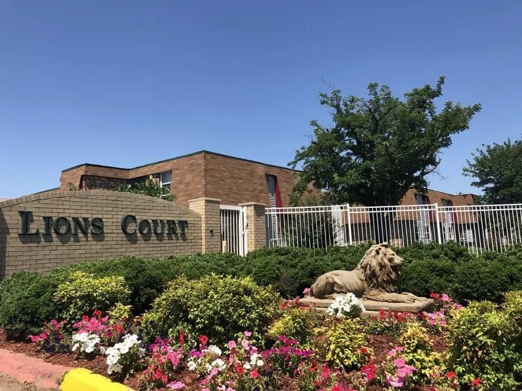 Lions Court sign at the main gated entrance of Lions Court Apartments with a statue of a lion and a flower bed | Wichita Falls, Texas