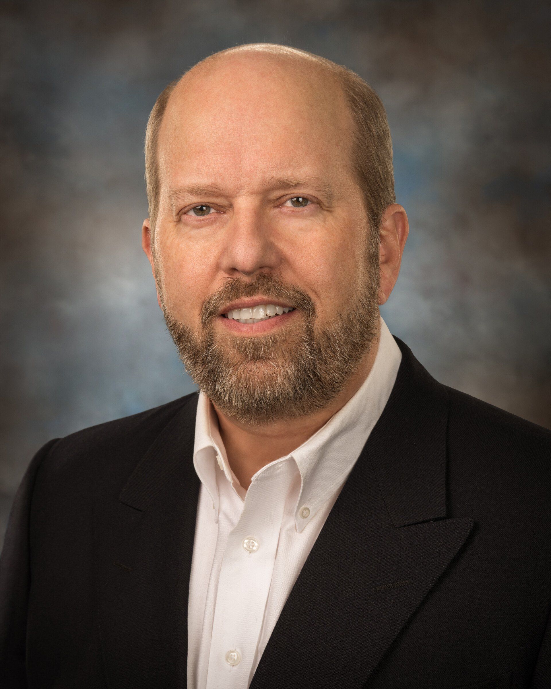A bald man with a beard wearing a suit and white shirt