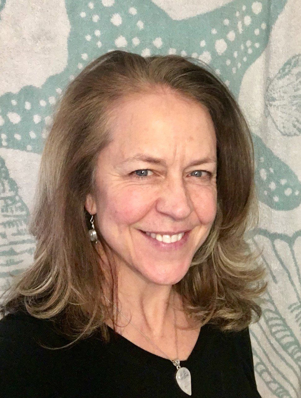 A woman wearing a black shirt and earrings is smiling for the camera.