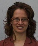 A woman wearing glasses and a red jacket is smiling for the camera.