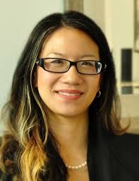 A woman wearing glasses and a black blazer is smiling for the camera