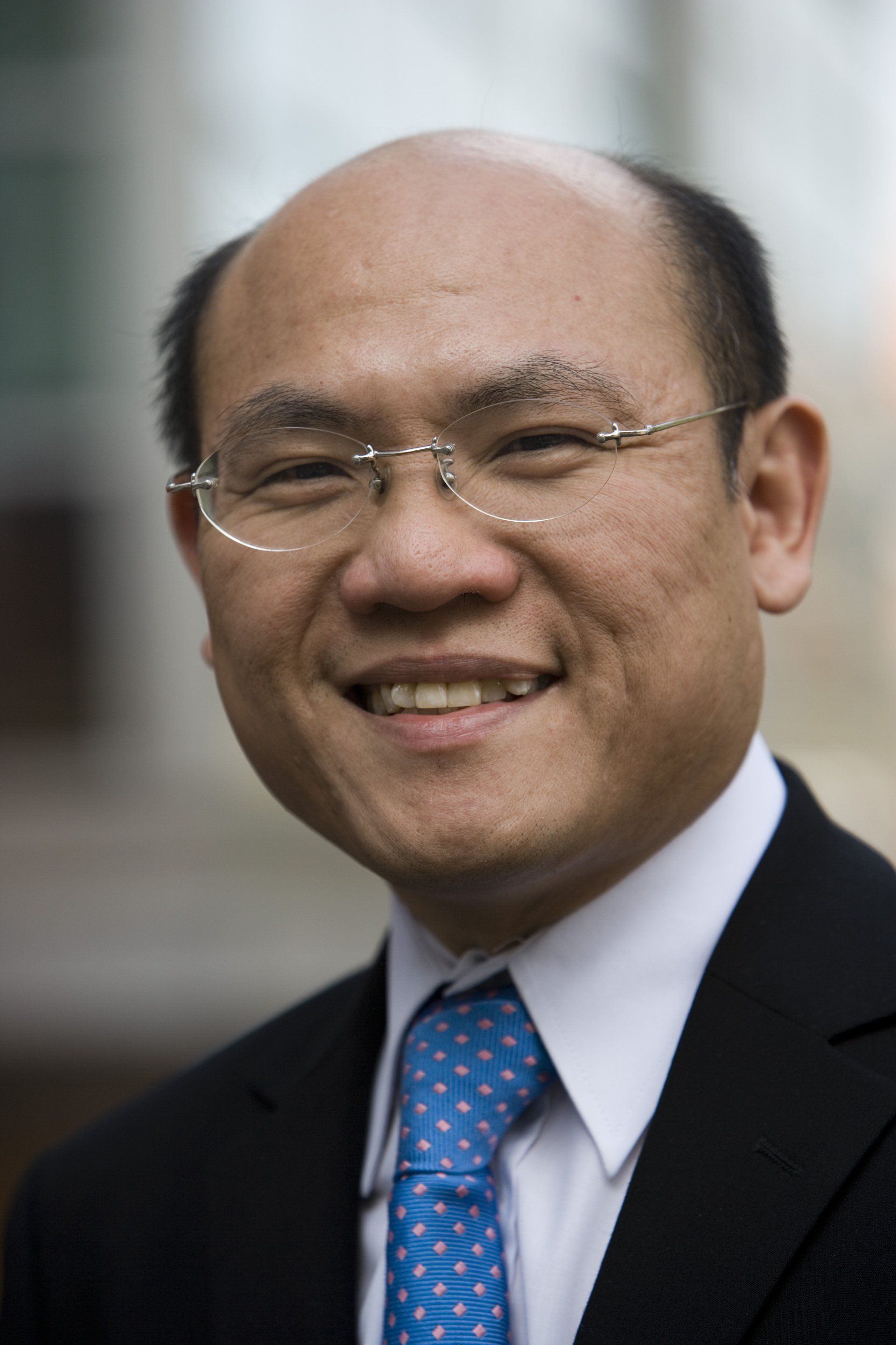 A bald man wearing glasses and a blue tie is smiling for the camera.