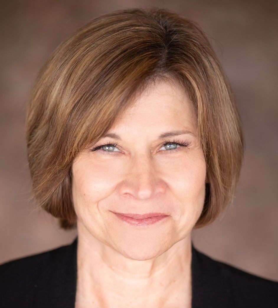 A woman with short brown hair and blue eyes is smiling for the camera.
