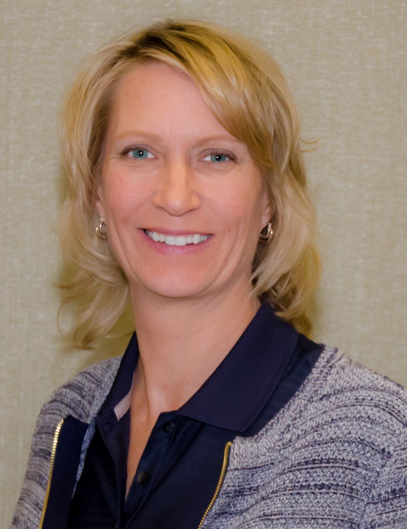 A woman with blonde hair and blue eyes is smiling for the camera