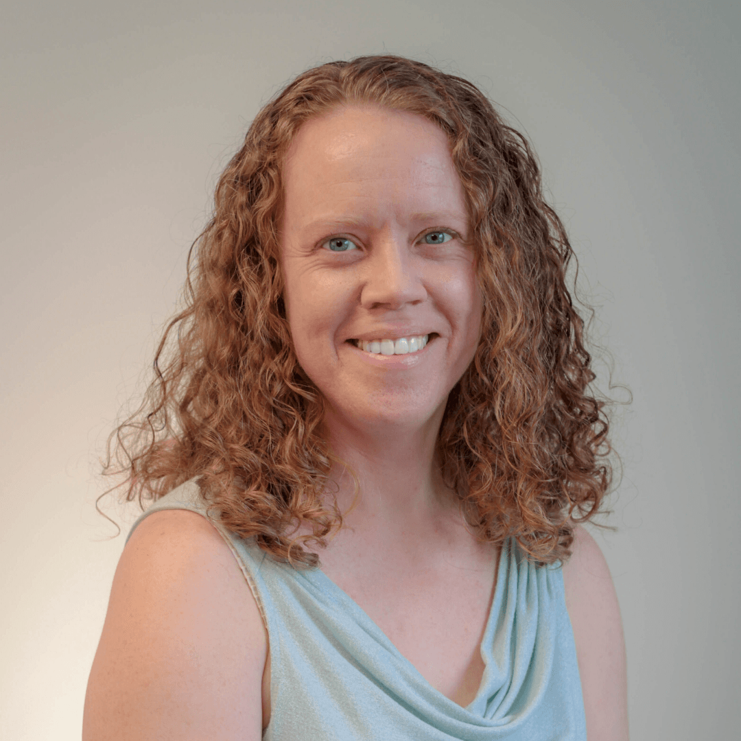 A woman with curly hair is smiling and wearing a blue tank top.