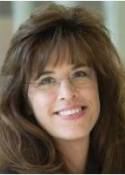 A woman with long brown hair and glasses is smiling for the camera.