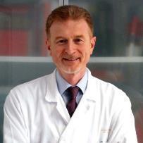 A man in a lab coat and tie is smiling for the camera.