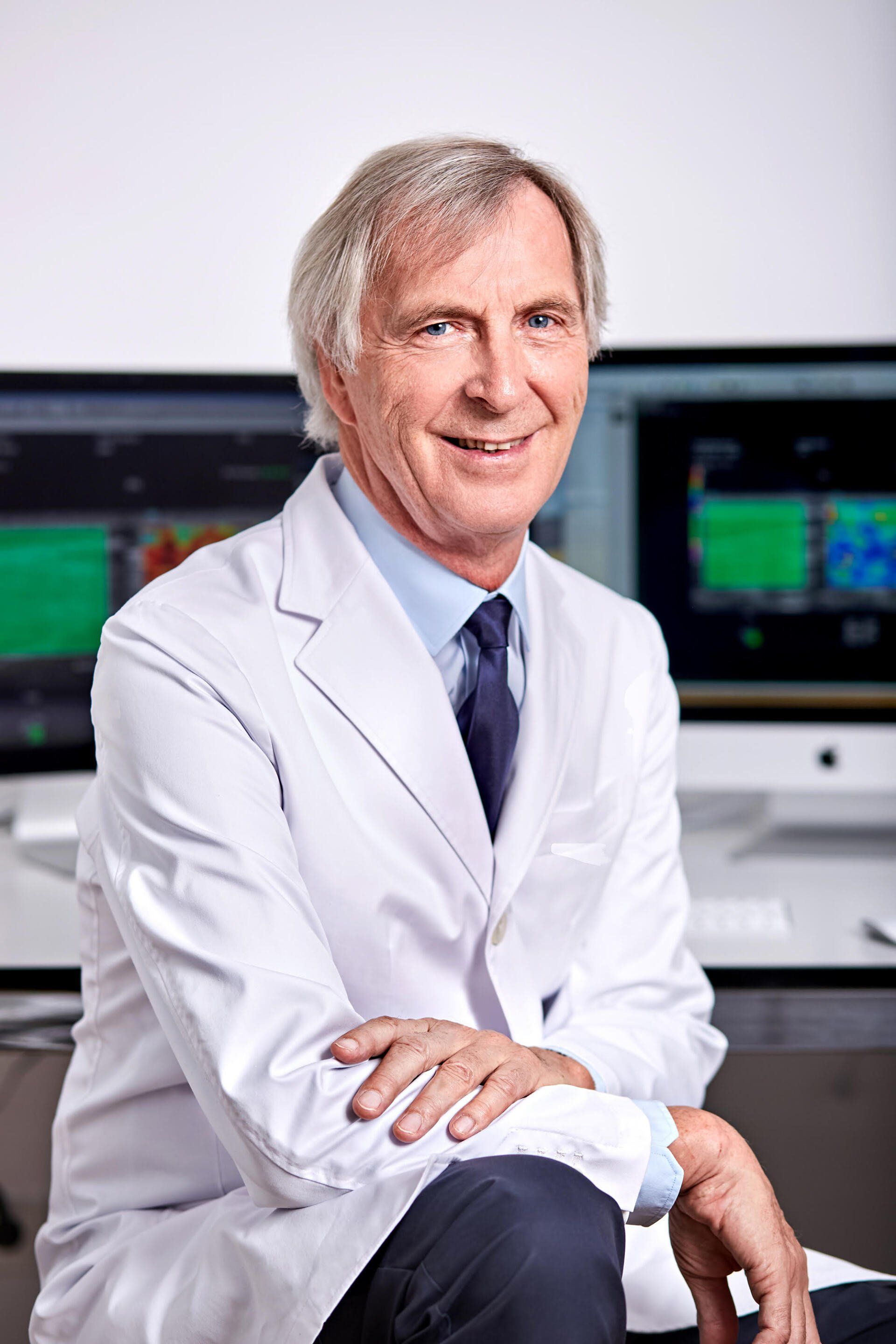 A man in a white coat and tie is sitting in front of a computer.