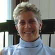 A woman wearing a blue turtleneck and earrings is smiling for the camera.