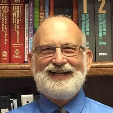 A man with a beard and glasses is smiling in front of a bookshelf.