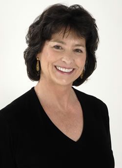 A woman wearing a black shirt and gold earrings smiles for the camera.
